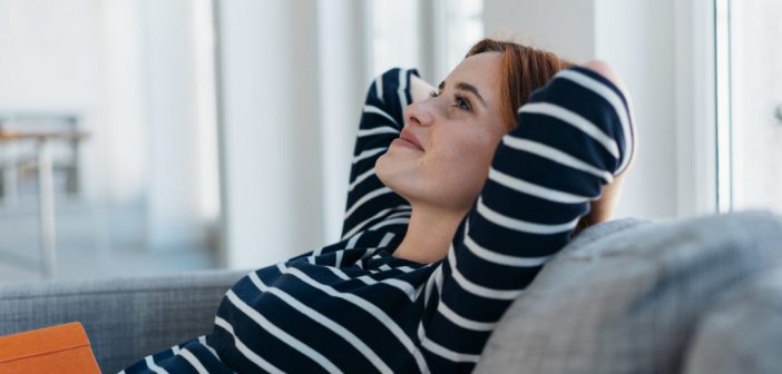 Saving Money When You Live Alone Women relaxing on grey sofa